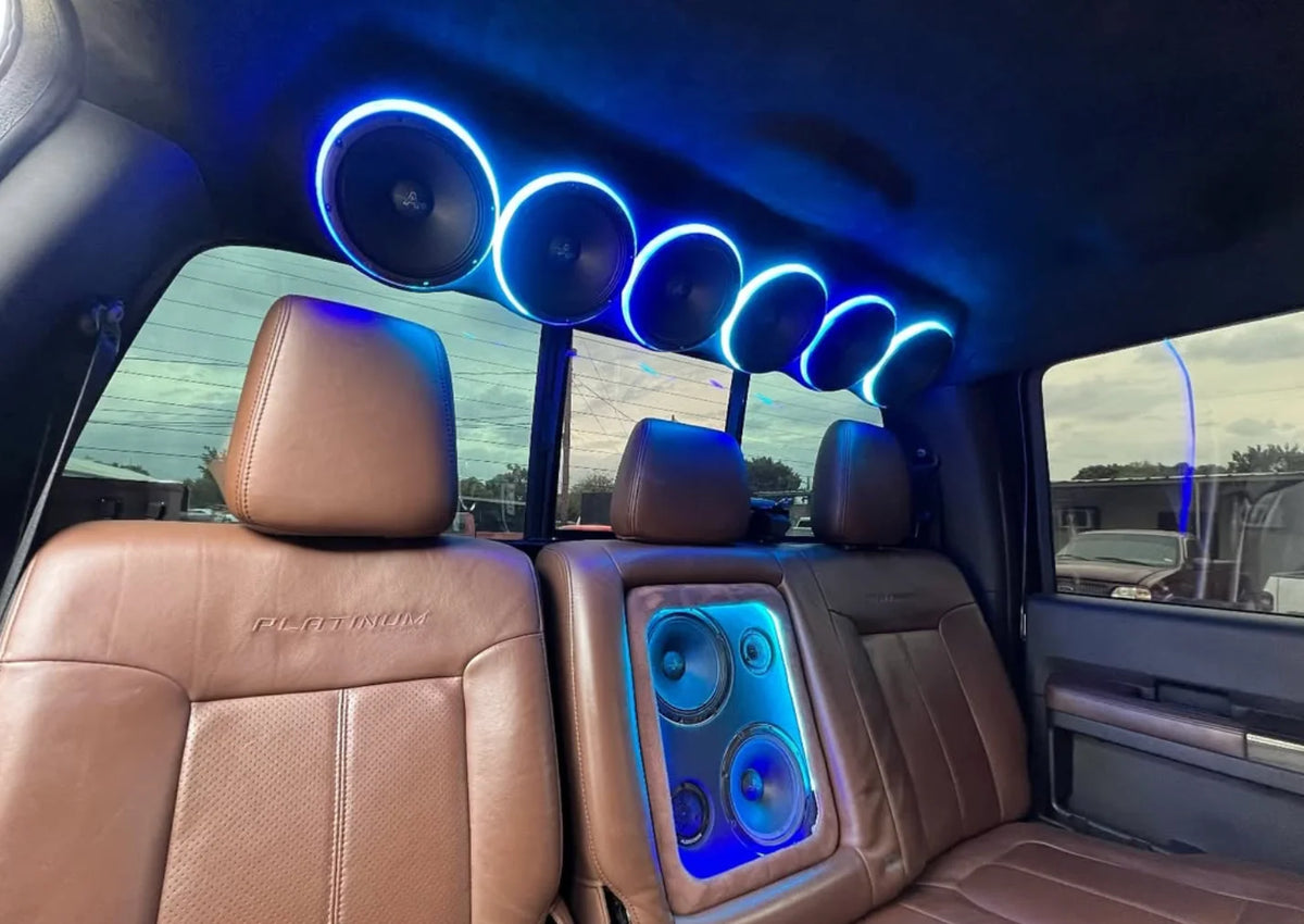 Car audio speaker rings with blue LED glow along headliner, several circular drivers