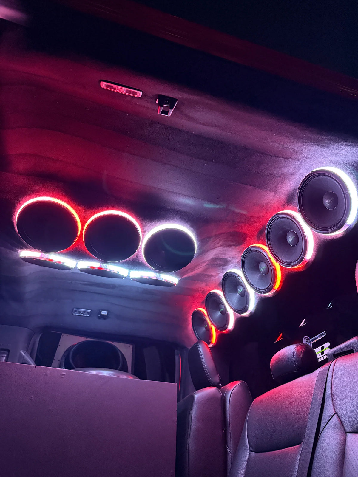 Car audio speaker rings with red and white LED glow, row of circular drivers overhead