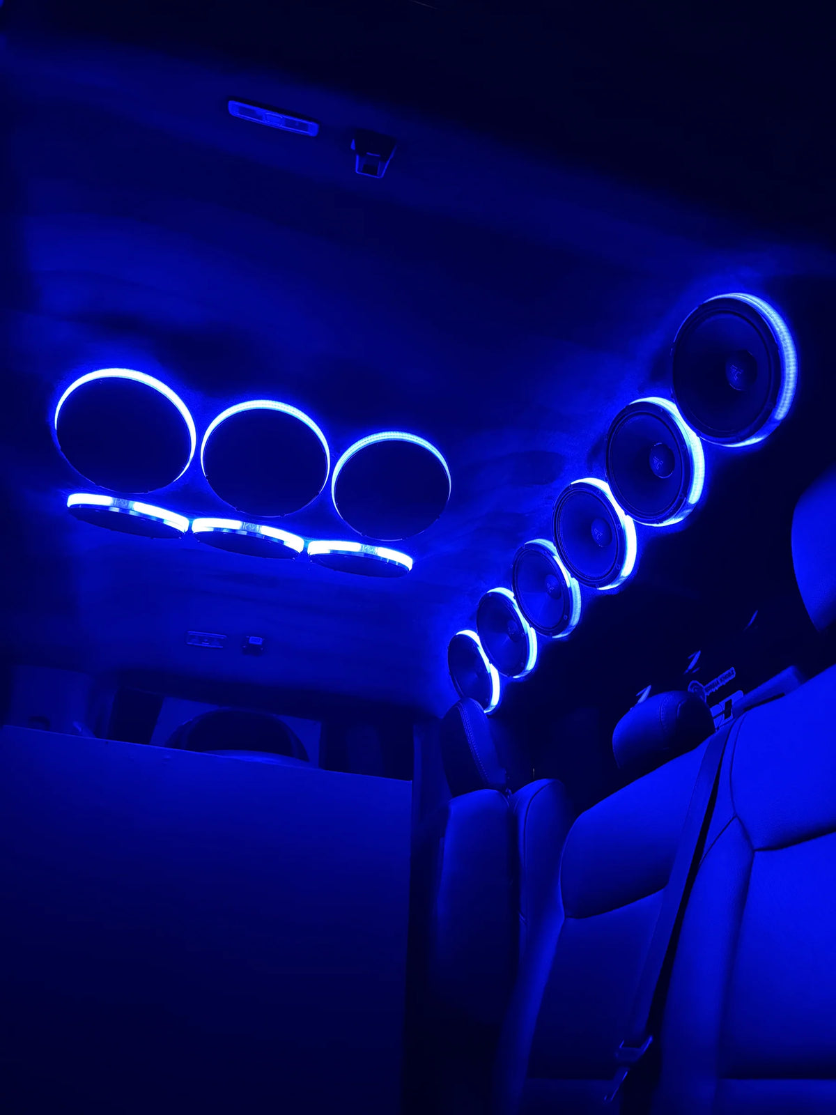 Car audio speaker rings with blue LED halos, multiple circular drivers along ceiling